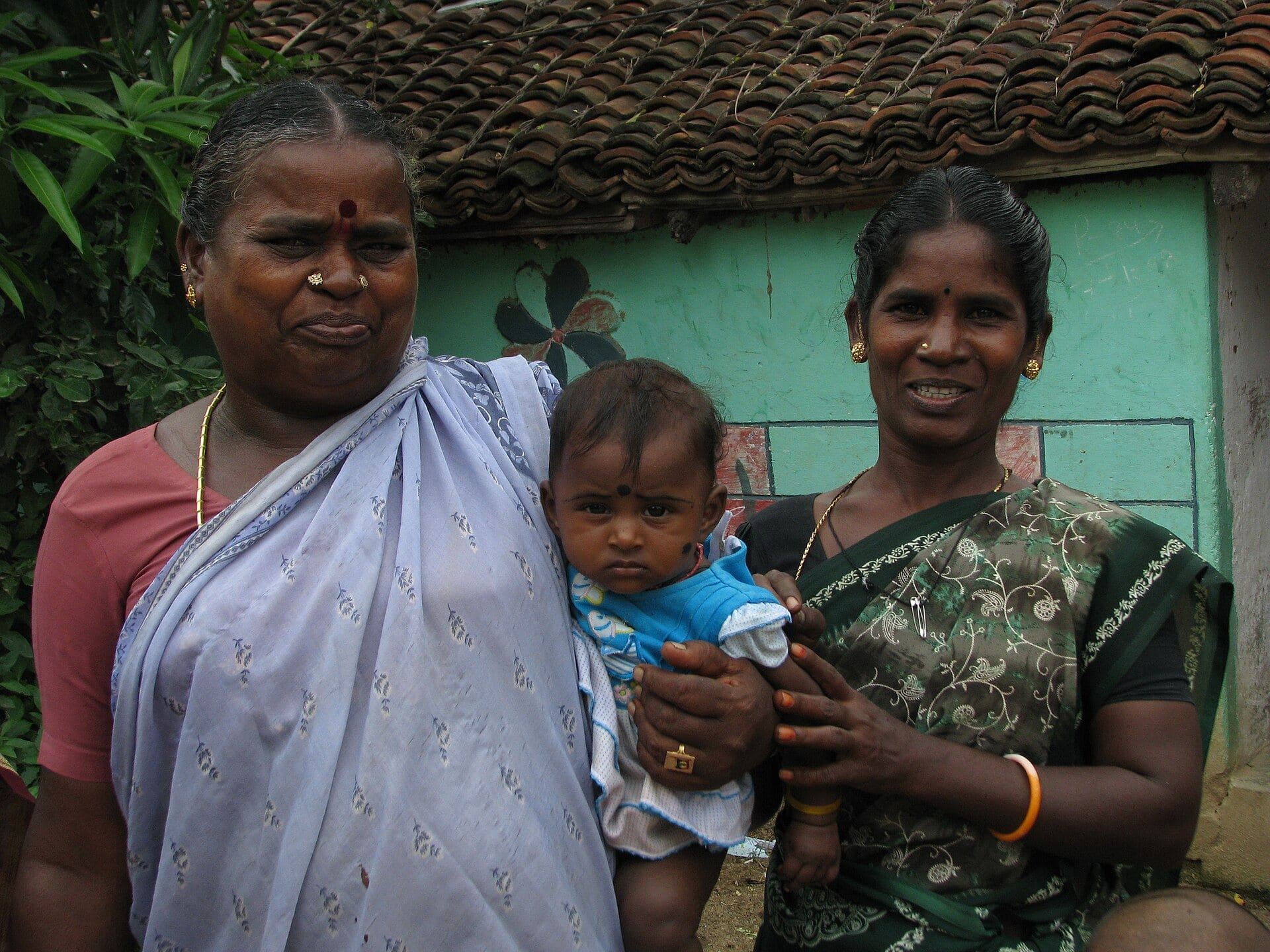 Two women and a baby outside their home