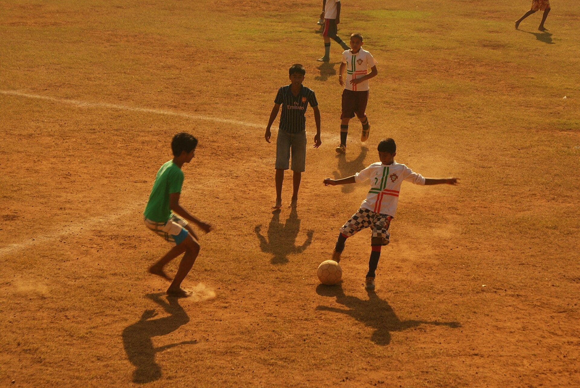 Boys playing football on a dusty ground